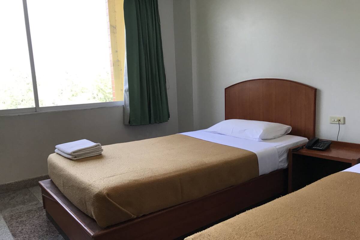 Habitación de hotel con una cama individual, una mesita de noche con teléfono y una ventana con cortina.