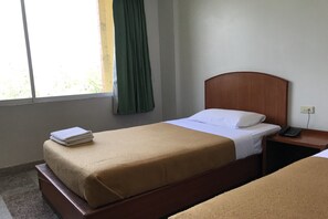 A hotel room with a single bed, a bedside table with a phone, and a window with a curtain.