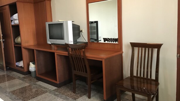 Un bureau en bois, une télévision, un miroir et une chaise se trouvent dans une pièce dont le sol est recouvert de carreaux.