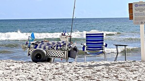 A beach scene with a fishing cart, a striped beach chair, and a sign about beach cleanliness.