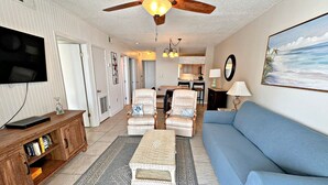 A living room with a blue sofa, a white armchair, a wicker coffee table, and a ceiling fan.