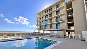 A multi-story hotel with a pool area, balconies, and a view of the beach.