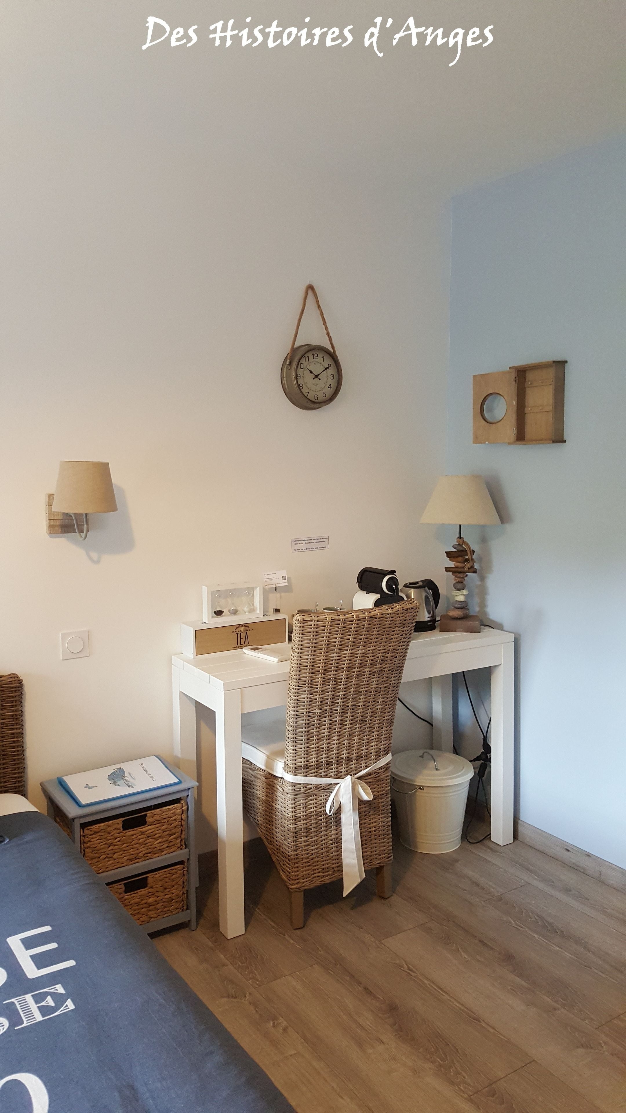 Una habitación acogedora con una silla de mimbre, un pequeño escritorio con una lámpara, un reloj de pared y un armario de madera.