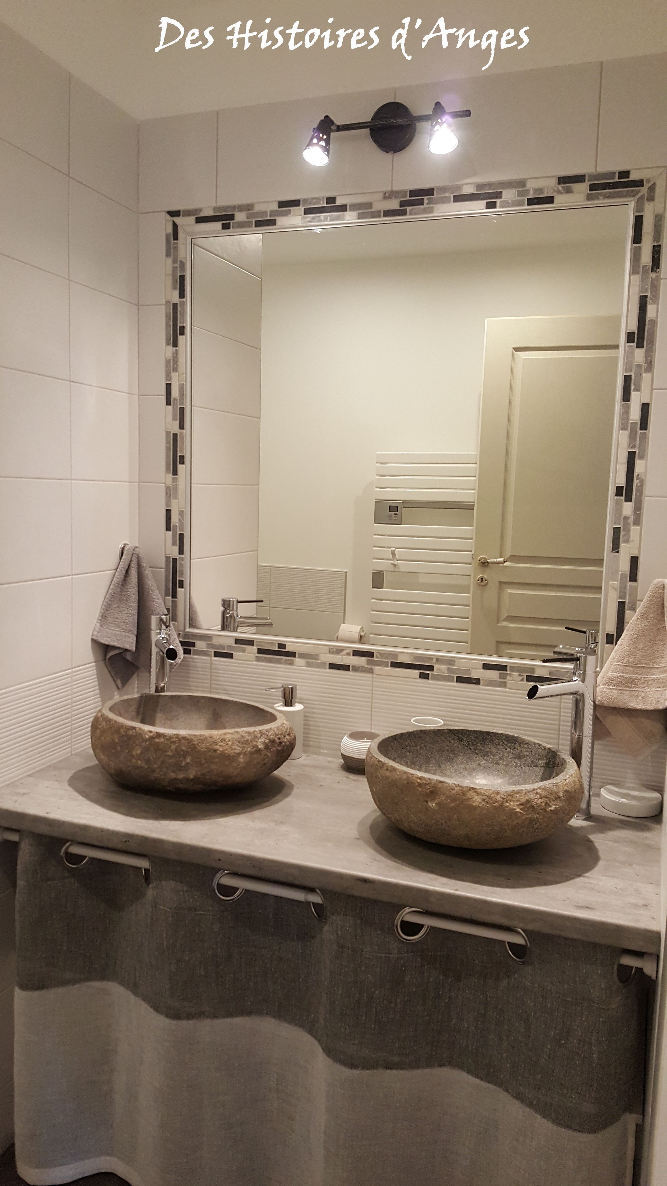 A bathroom with two stone sinks, a mirror with a mosaic border, and a towel rack.