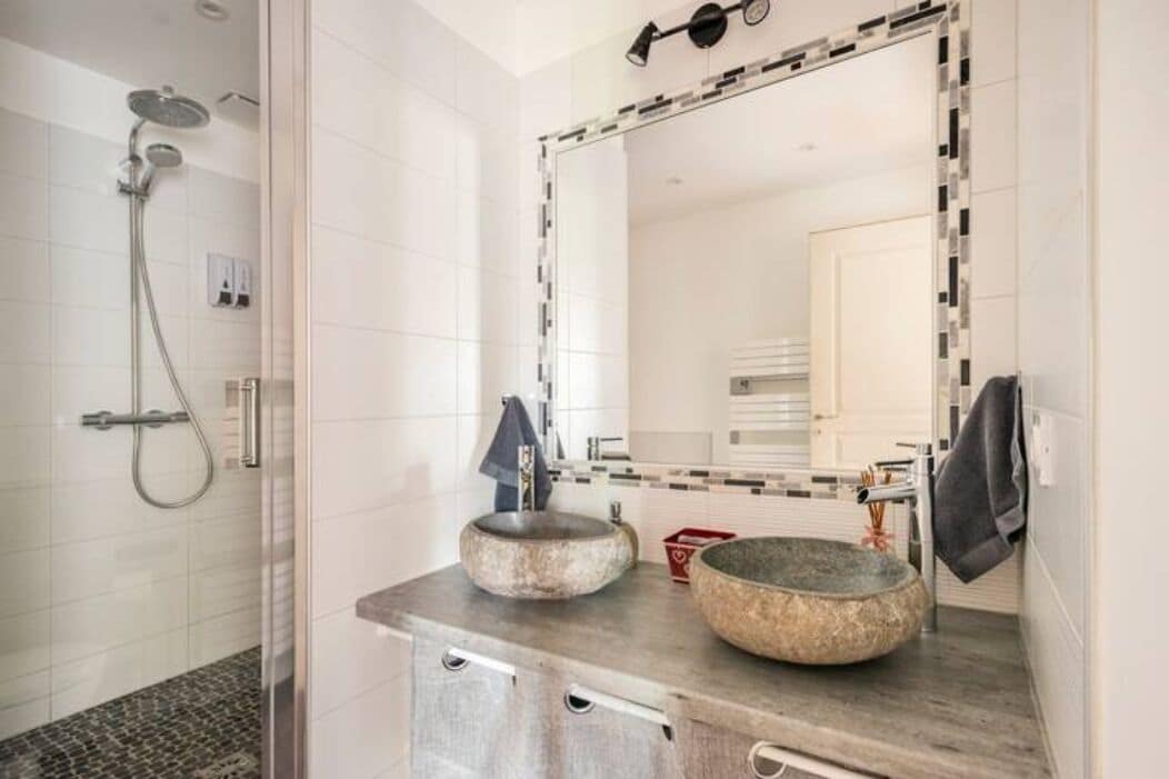 A modern bathroom with a glass-enclosed shower, a round sink with a stone basin, and a large mirror with a decorative frame.