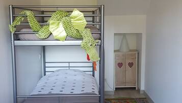 A bunk bed with a green dinosaur decoration, a wooden cabinet with heart designs, and a colorful play mat on the floor.