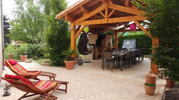 A covered outdoor dining area with wooden tables and chairs, a hanging chair, and potted plants.