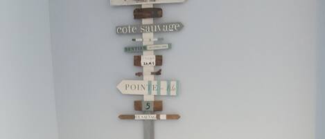 A corner with a wicker chair, a small basket, and a wall-mounted sign with directional text.
