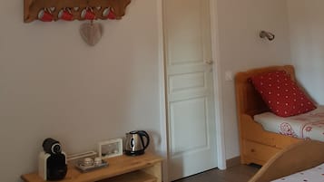 Et hyggeligt soveværelse med synlige træbjælker, en seng med pude med prikker, et natbord med elkedel og en reol med bogstaverne 'HOME' og røde kopper.