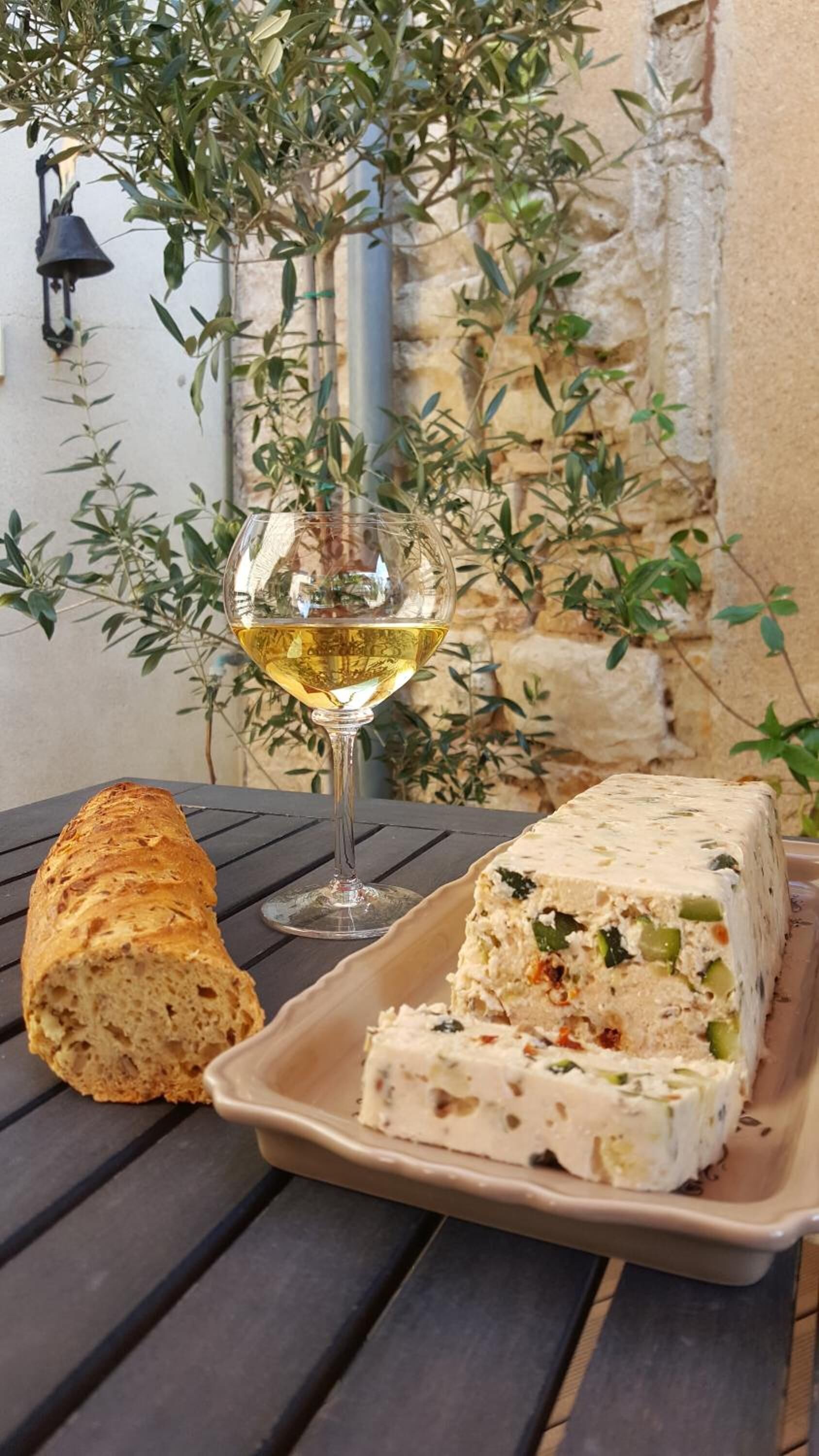 A table with a loaf of bread, a glass of white wine, and a plate of cheese.