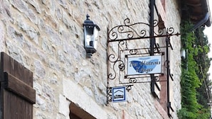 A stone building with a wooden door, a sign reading "Les Histoires d'Anges," and a parking sign.