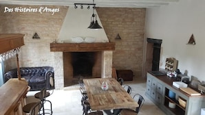 A rustic room with a stone wall, a fireplace, a wooden table with chairs, a leather sofa, and a kitchen area with cabinets and a countertop.
