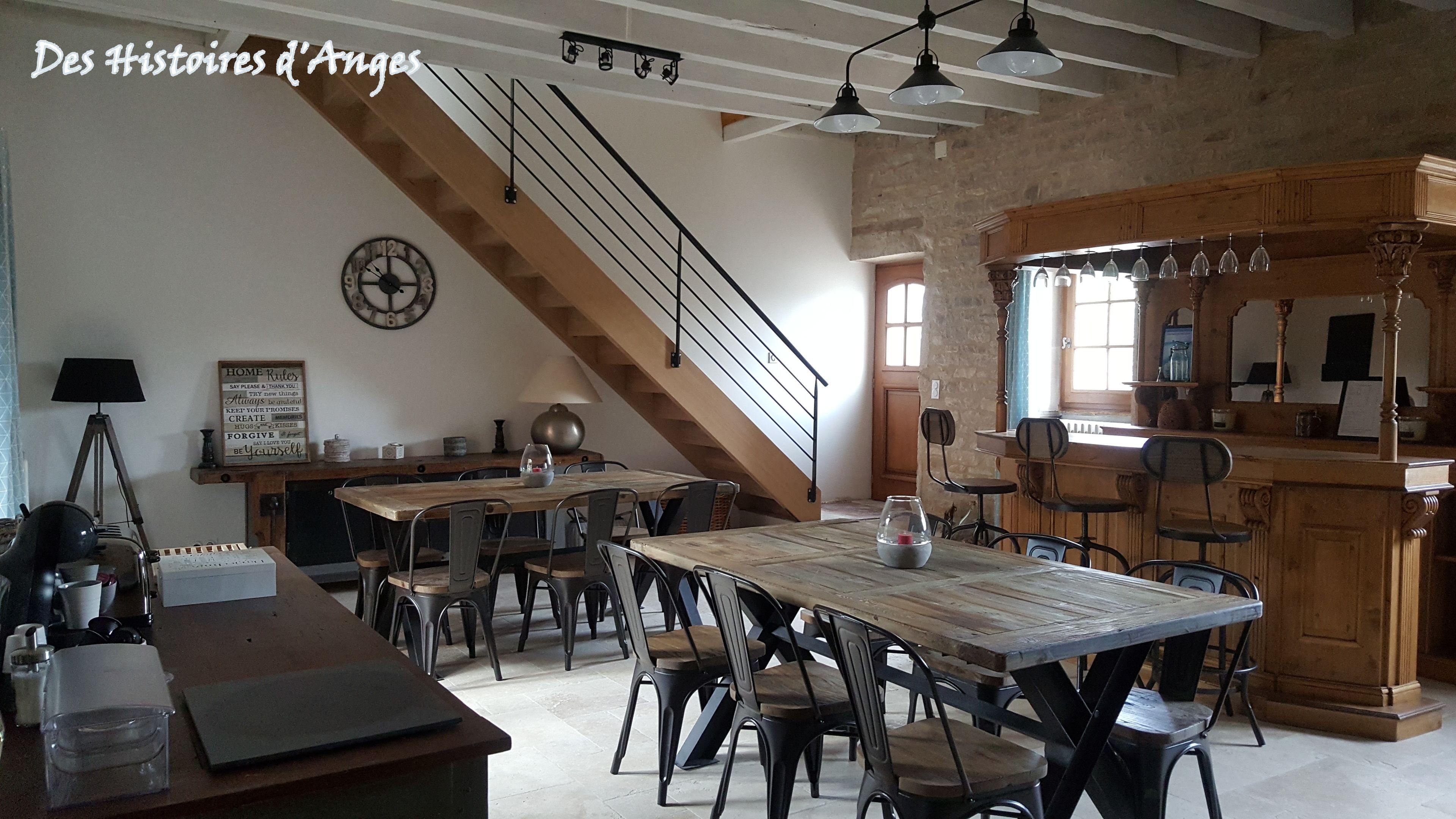 A spacious kitchen with wooden cabinets and a large island, a dining area with a rustic wooden table and metal chairs, and a staircase leading to an upper level.