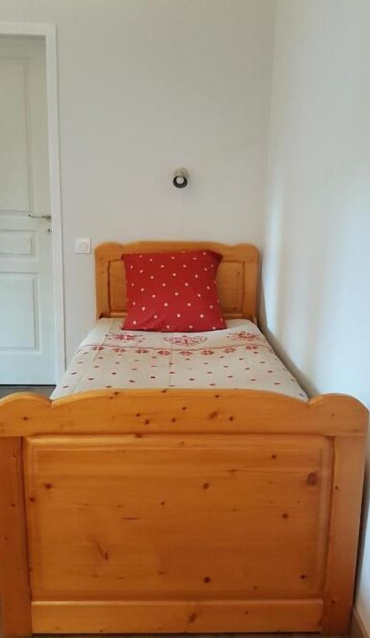 Una cama de madera pequeña con un cojín rojo de lunares y una colcha estampada con motivos florales.