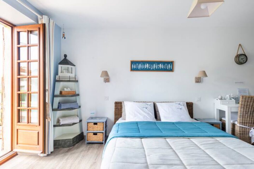 A bedroom with a bed, a nightstand, a shelf unit, a clock, and a window with curtains.