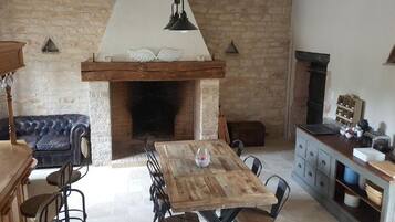 Una habitación rústica con pared de piedra, chimenea, mesa de madera con sillas, sofá de cuero y una zona de cocina con armarios y encimera.