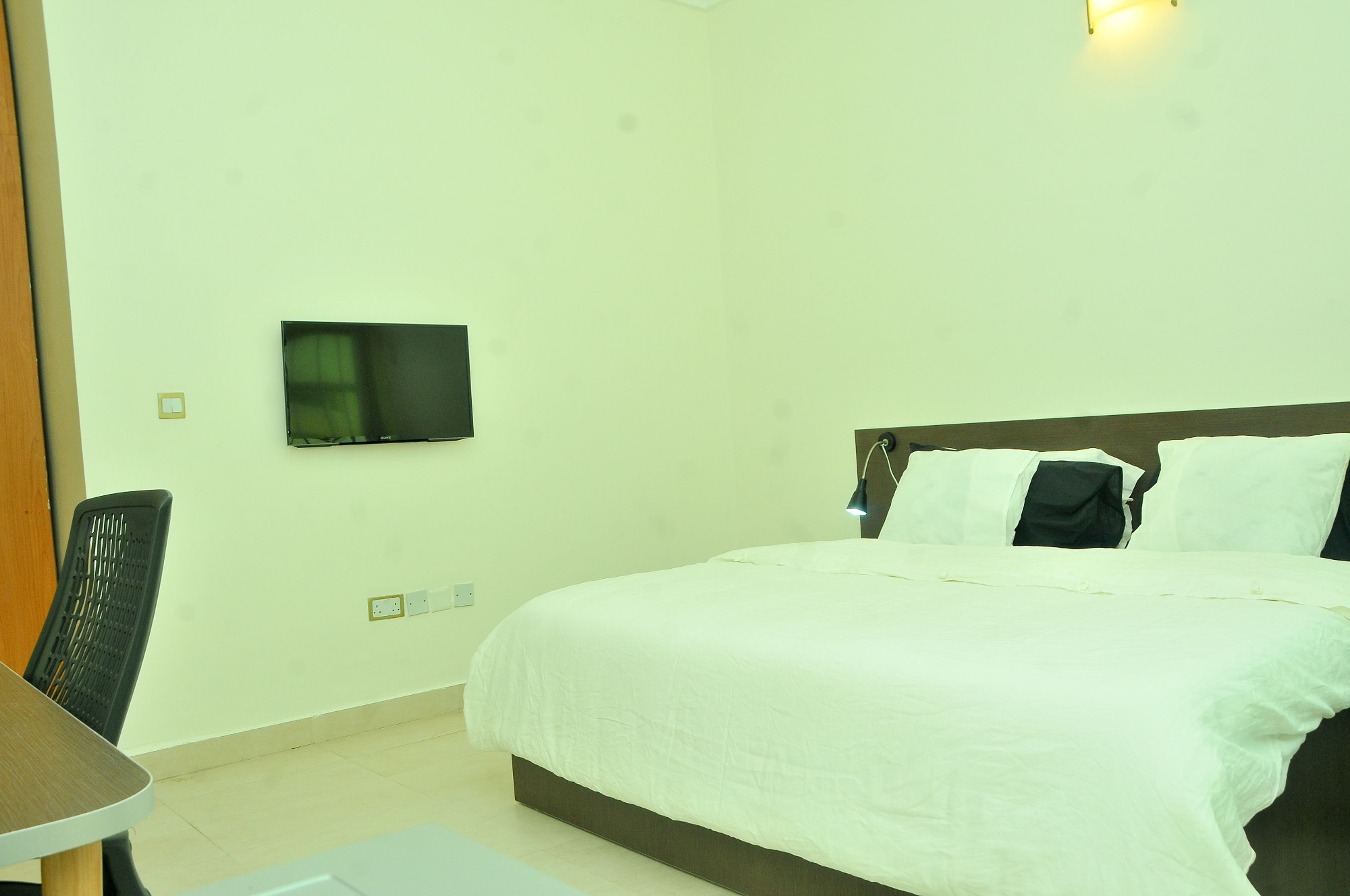 A hotel room with a bed, a desk, and a TV mounted on the wall.
