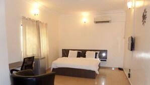 A hotel room with a bed, a desk, a chair, and an air conditioning unit. - Nordic Hospitality Hotel (Abuja)