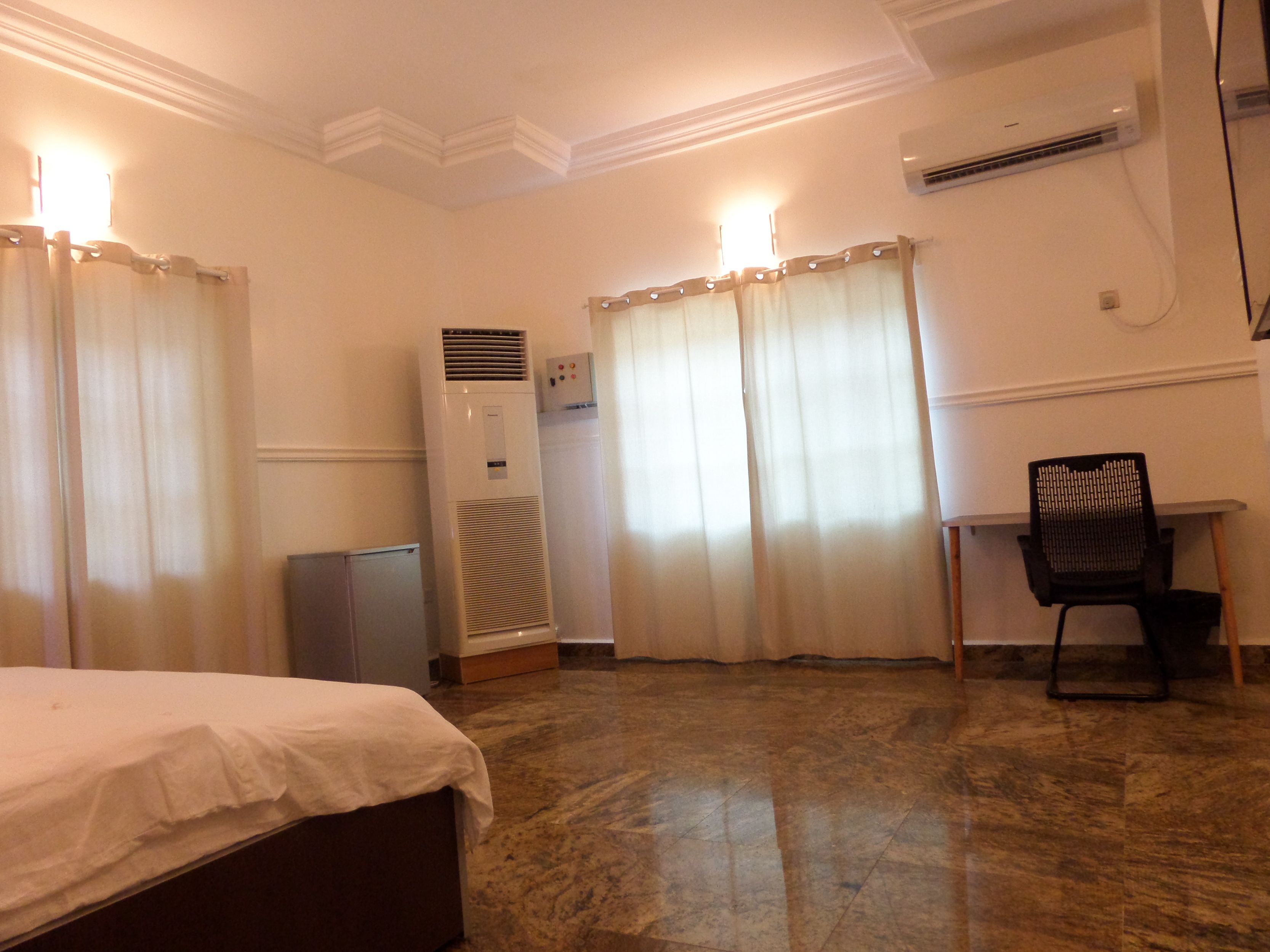A hotel room with a bed, a desk, an air conditioner, and a water heater.