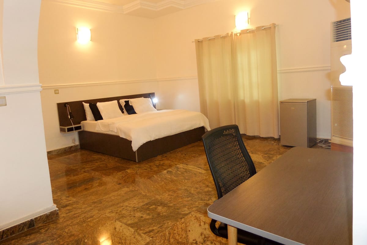 A hotel room with a bed, a desk, a chair, a heater, and a curtain.