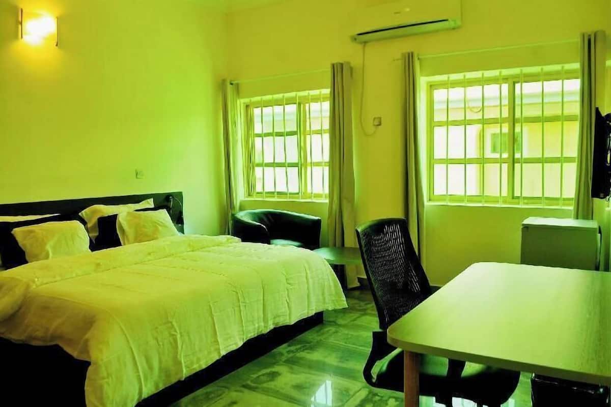 A hotel room with a bed, a desk, a chair, and two windows with curtains.
