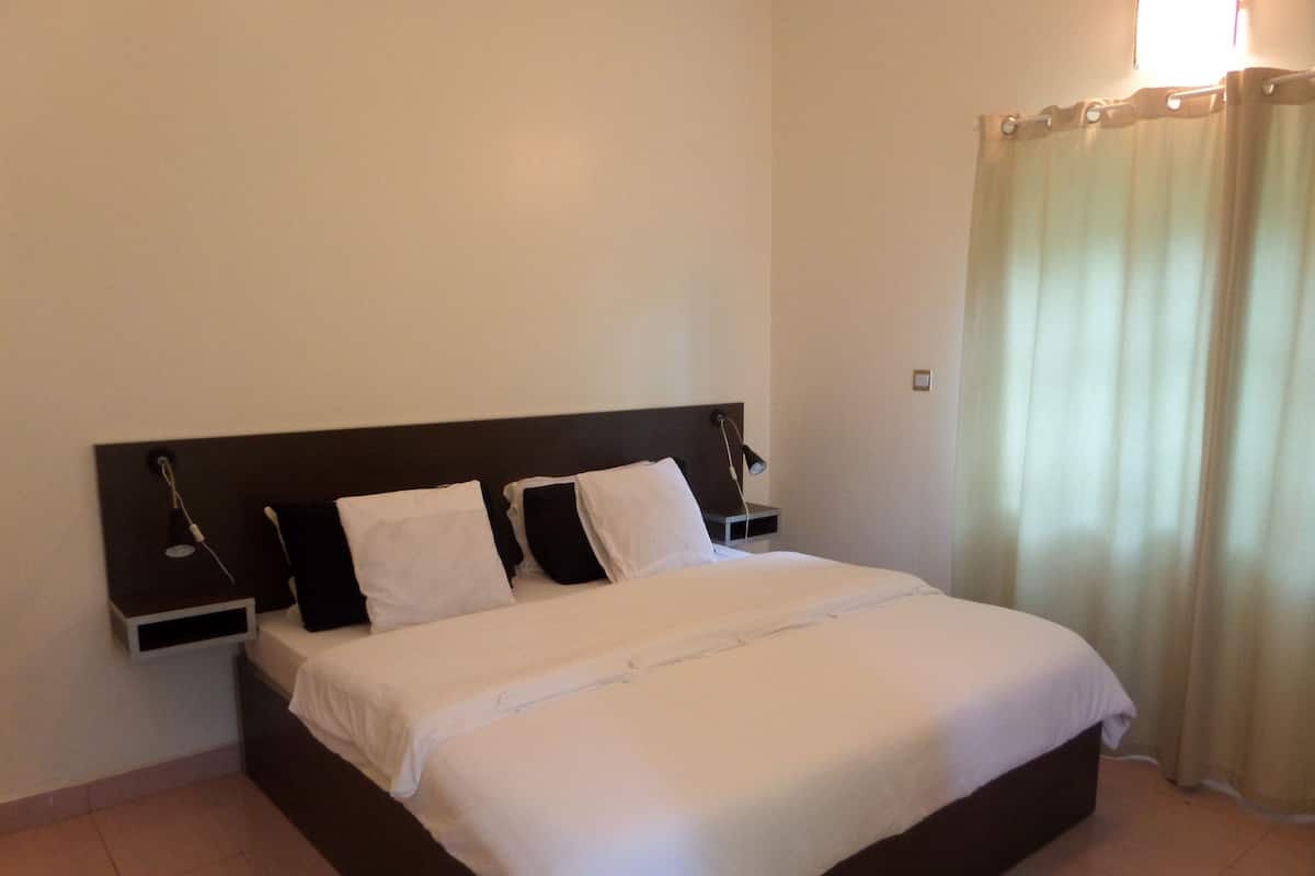 A neatly made bed with white bedding, a dark headboard, and a bedside table with a lamp.