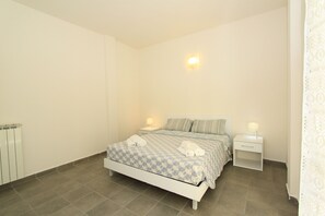 A bedroom with a bed, two bedside tables, a nightstand, and a wall-mounted light fixture. - Villa Pineta Apartments (Comacchio)
