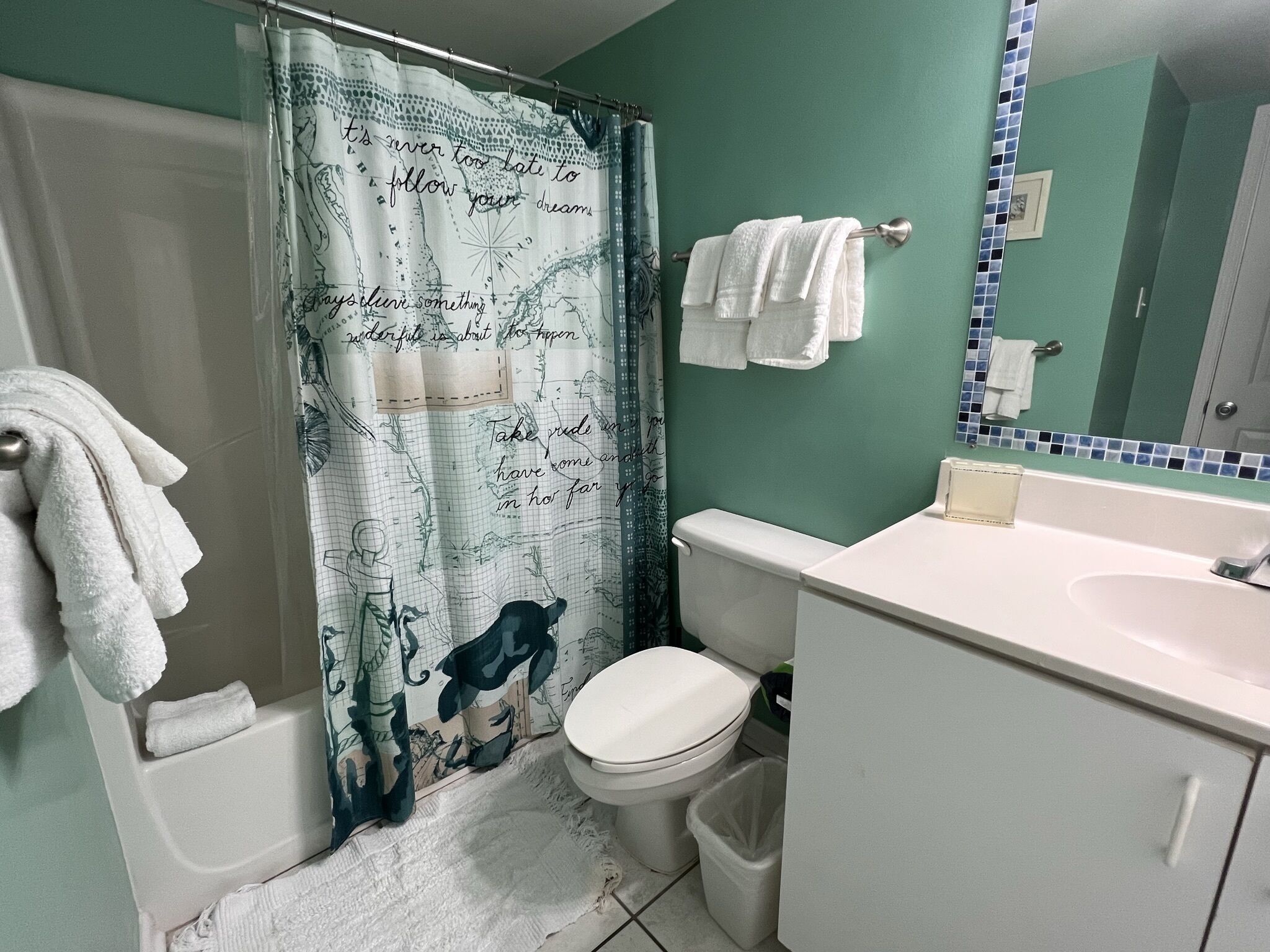 A bathroom with a shower curtain featuring a nautical map design, a toilet, a sink, and a mirror with a mosaic backsplash.