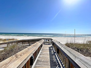 A wooden boardwalk leading to a beach with a clear sky and ocean view.