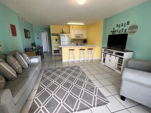 Una sala de estar con un sofá, televisor y una zona de cocina con barra.