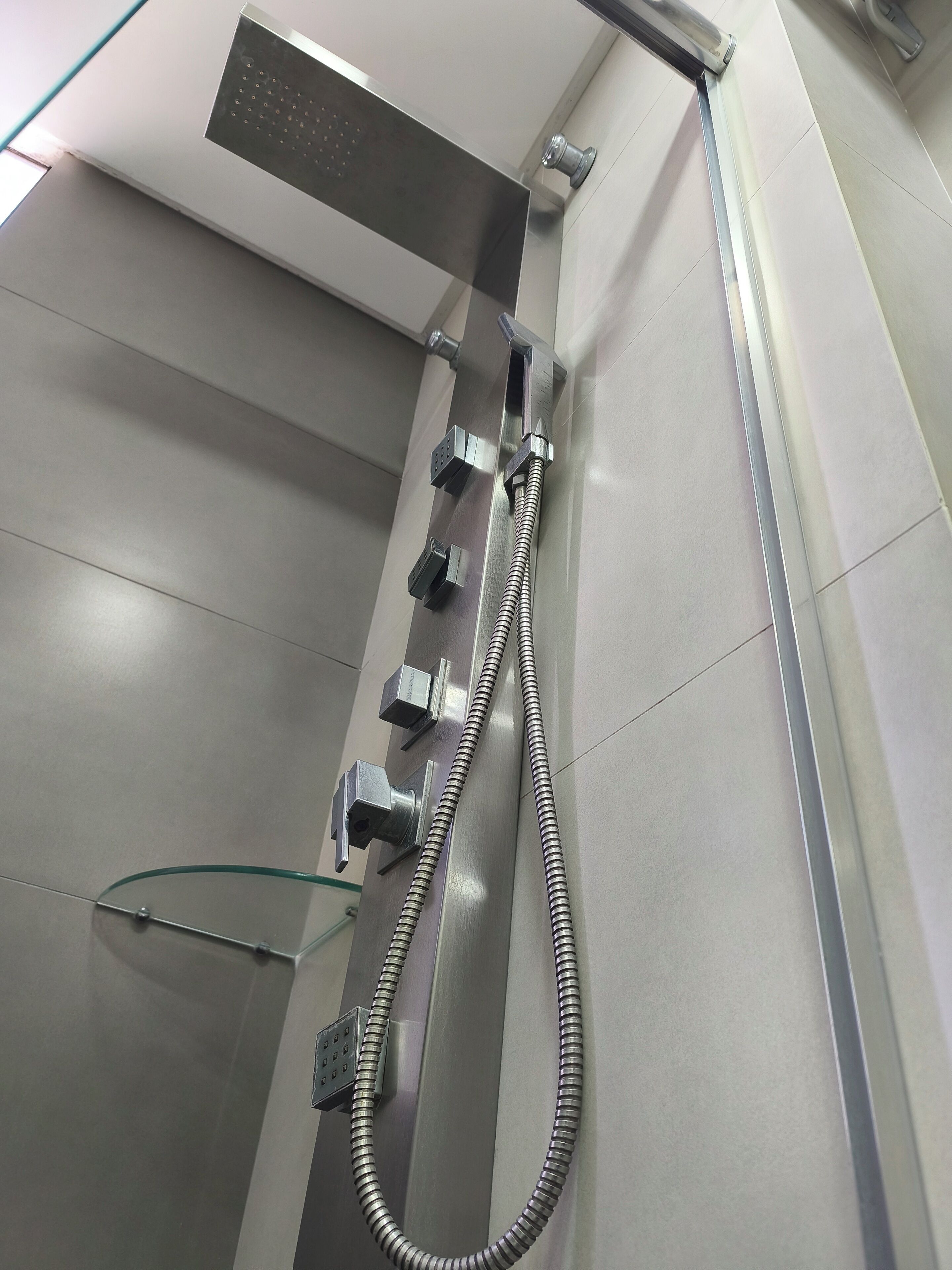 A modern shower with a handheld showerhead, a fixed showerhead, and a control panel.