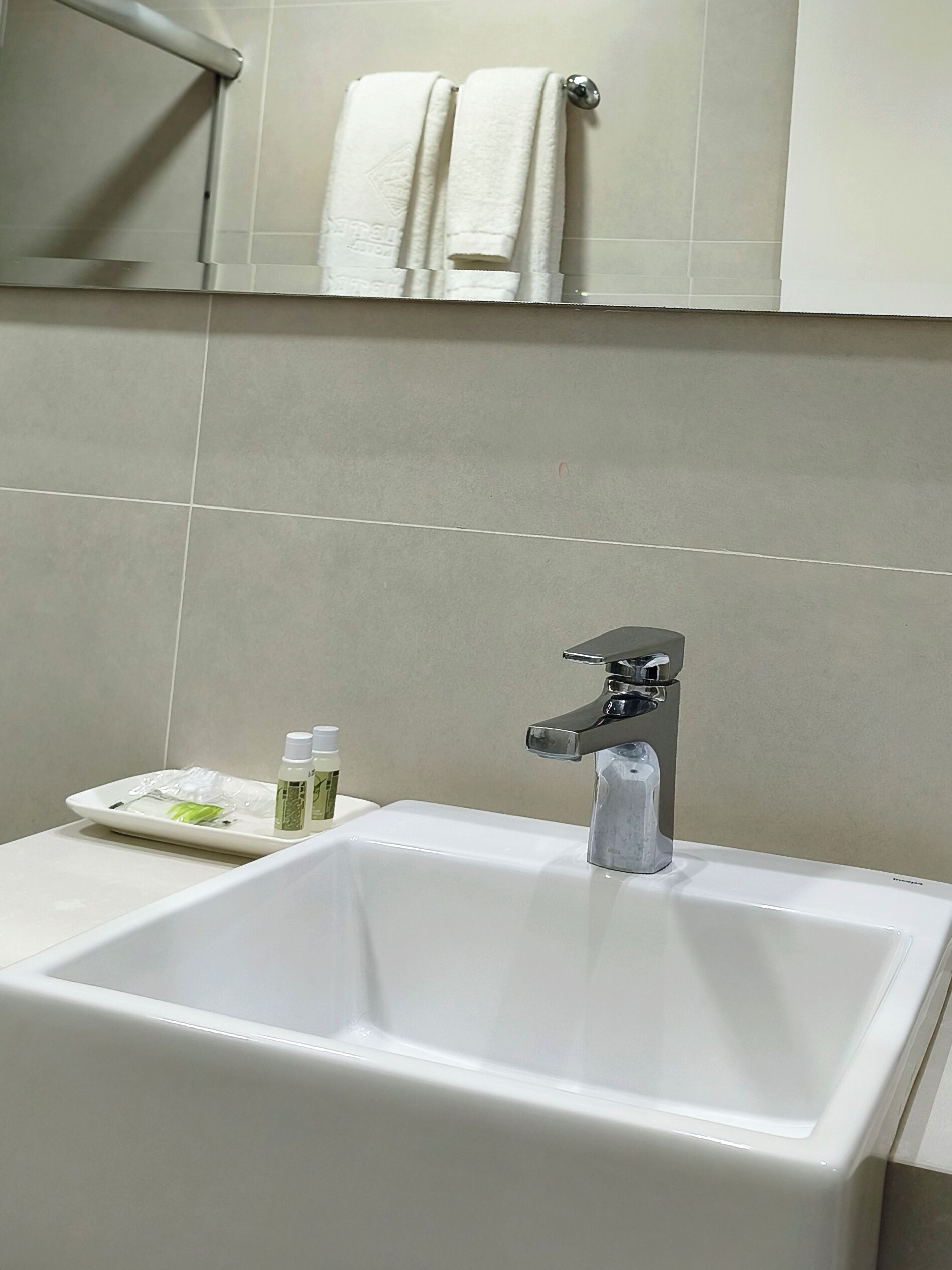 A bathroom with a white sink, a mirror, and two towels hanging on the wall.