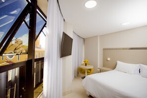 A hotel room with a bed, a small round table with a vase of flowers, a TV mounted on the wall, and a window with curtains. - Hotel San Pietro (Pato Branco)