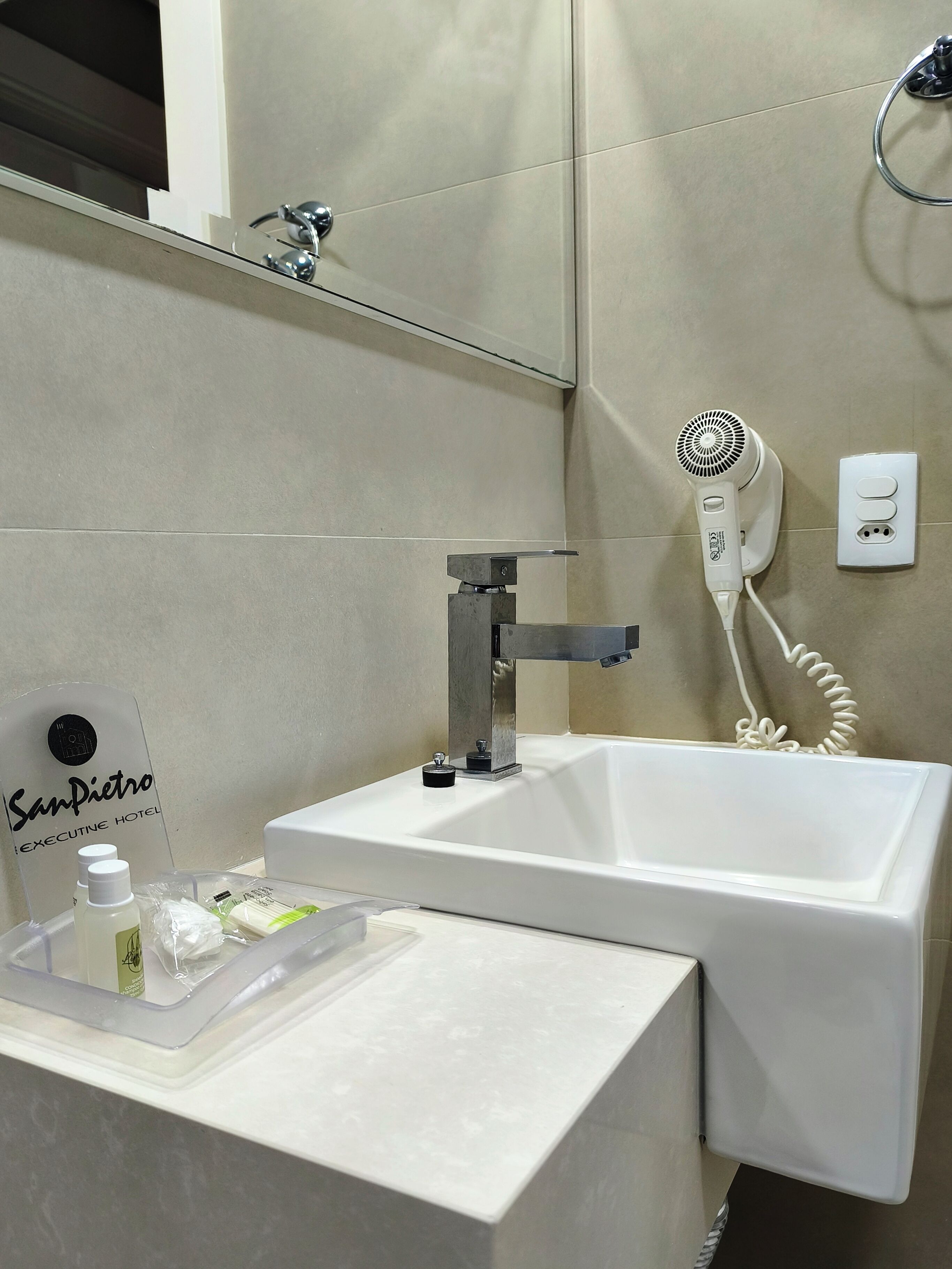 Un baño con un lavabo blanco, un secador de pelo de mano y un espejo sobre el lavabo.
