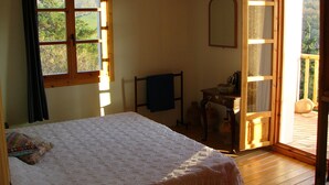 A bedroom with a bed, a desk, a chair, a mirror, and a sliding glass door leading to a balcony.