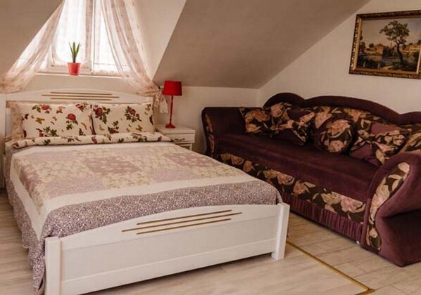 Un dormitorio con cama, sofá, mesita de noche, lámpara y ventana con planta.