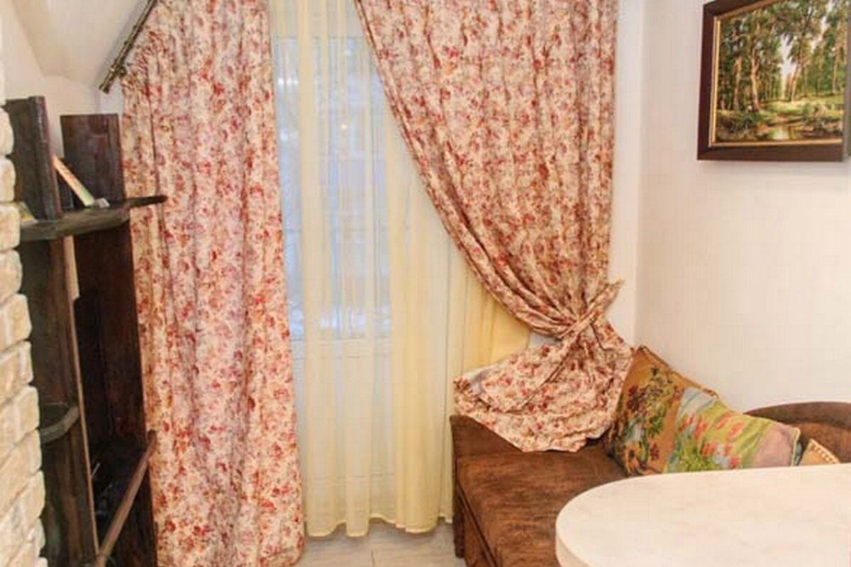 Un rincón acogedor con un sofá marrón, una mesa redonda y una ventana con cortinas florales.