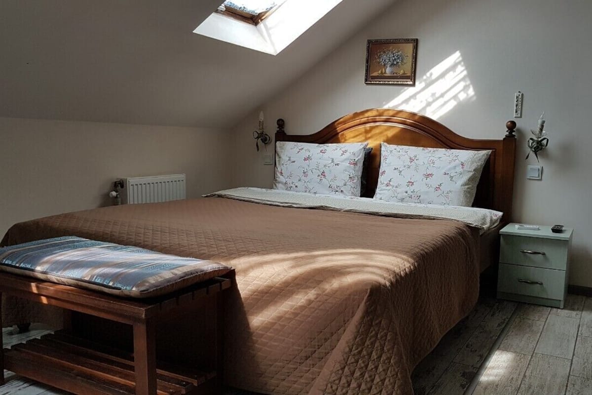 Ein Schlafzimmer mit einem hölzernen Bett, einem Nachttisch, einer Bank und einem Oberlicht.