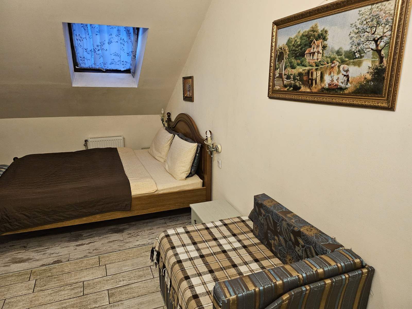 A bedroom with a bed, a small sofa, a painting, and a window.