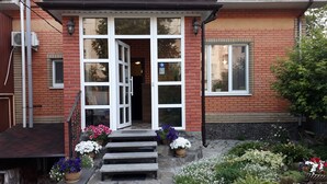 Een gebouw van baksteen met een witte ingang, stenen trappen en een tuin met verschillende bloemen.