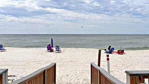 A beach with several blue and red lounge chairs, a wooden walkway, and a view of the ocean.