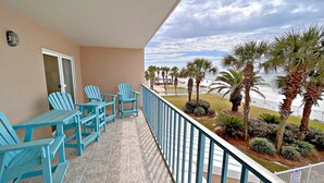 A balcony with turquoise chairs and a view of the beach and palm trees.