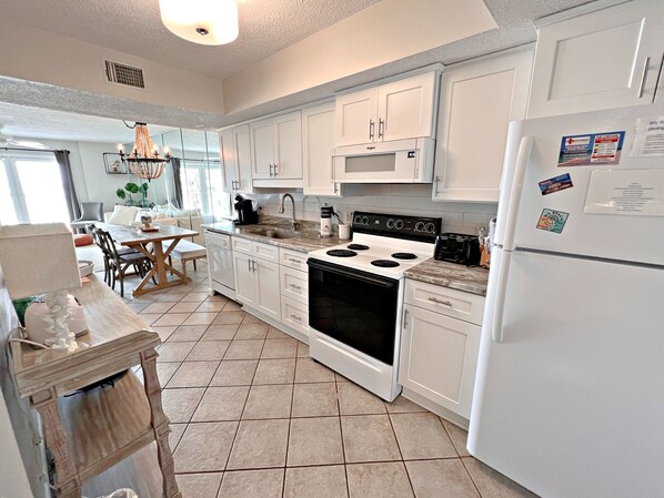 A modern kitchen with white cabinets, a stove, a refrigerator, and a dining area with a table and chairs.