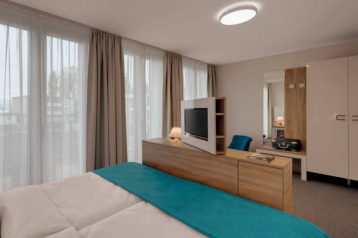 A hotel room with a bed, a desk with a flat-screen TV, a mirror, and a wardrobe.
