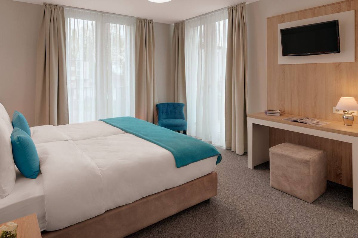 A hotel room with a bed, a desk, a chair, a TV, and a lamp.