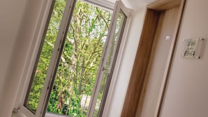 A hallway with a wooden door marked with the number 80, a window with a metal railing, and a view of trees outside. - Seereich Hotel & Pension (Lindau)