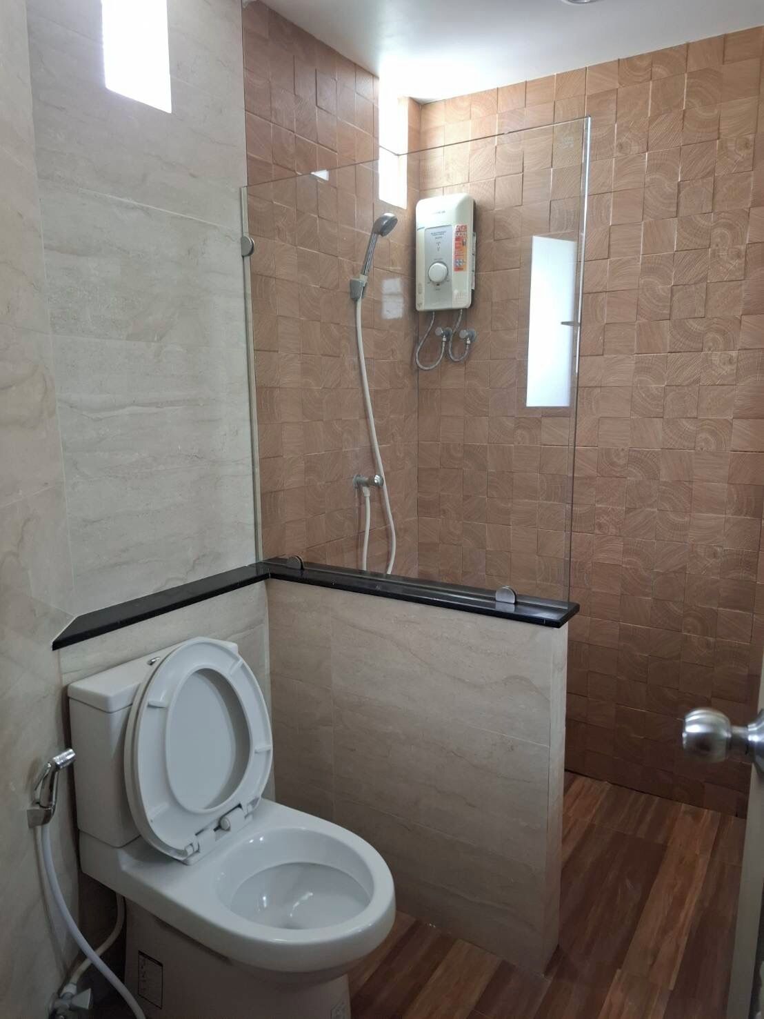 Casa de banho com sanita, chuveiro com divisória de vidro e painel de comandos na parede.