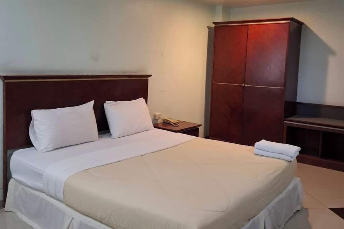 A hotel room with a large bed, a wooden wardrobe, a nightstand, and a telephone.
