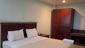 A hotel room with a large bed, a wooden wardrobe, a nightstand, and a telephone.