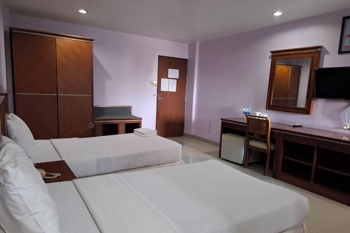 A hotel room with two beds, a desk, a chair, a TV, and a wardrobe.